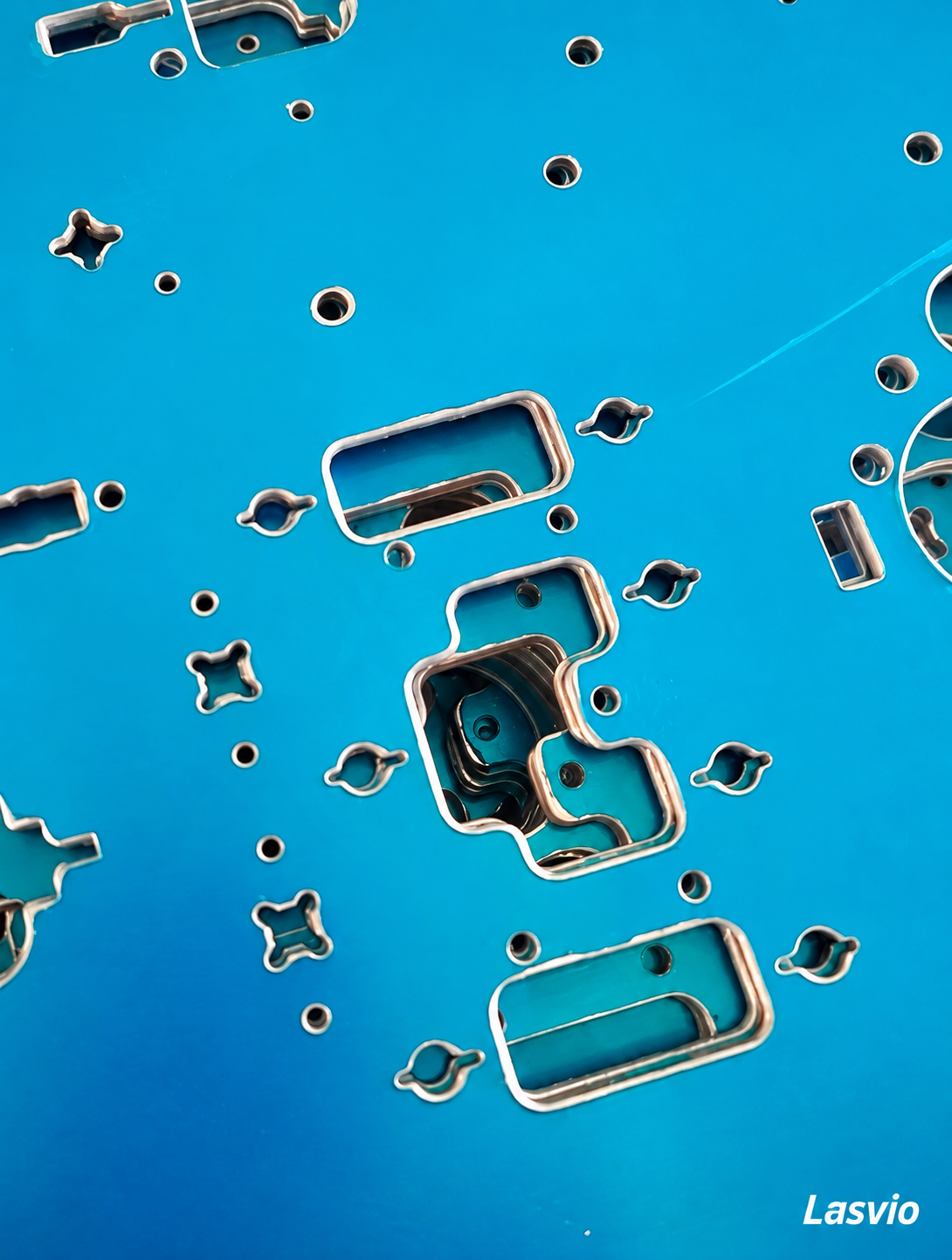 Sheet metal covered with blue protective film, showing circular holes, slots and exposed metal edges